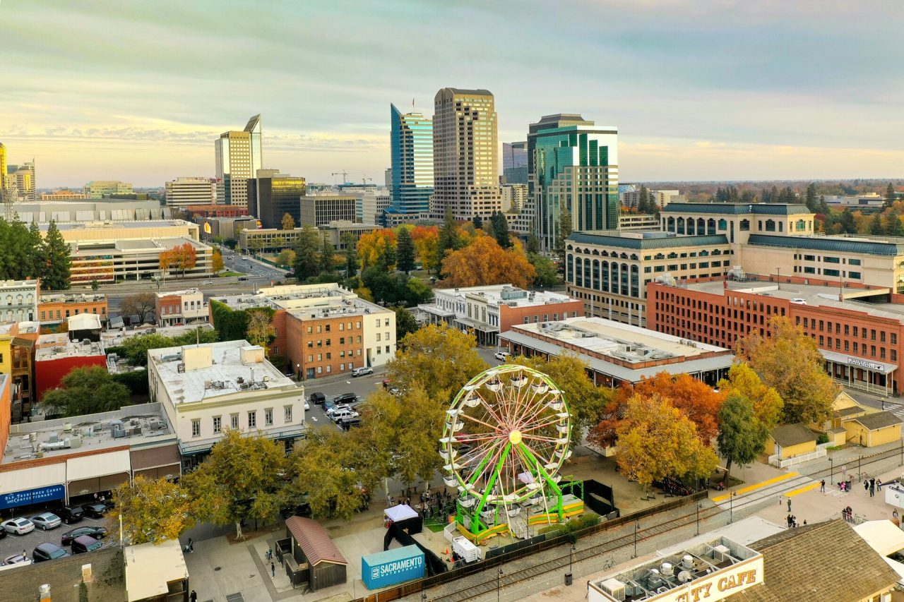 A large Ferris wheel located near city buildings on a bright, sunny daytime.