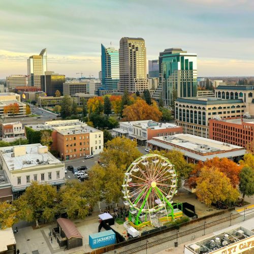 A large Ferris wheel located near city buildings on a bright, sunny daytime.