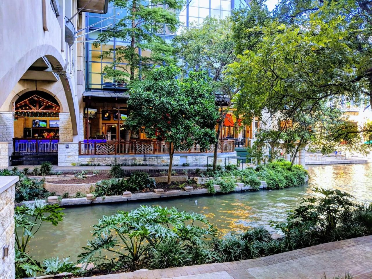 River flowing through a city alongside a tall residential building and lush green trees.
