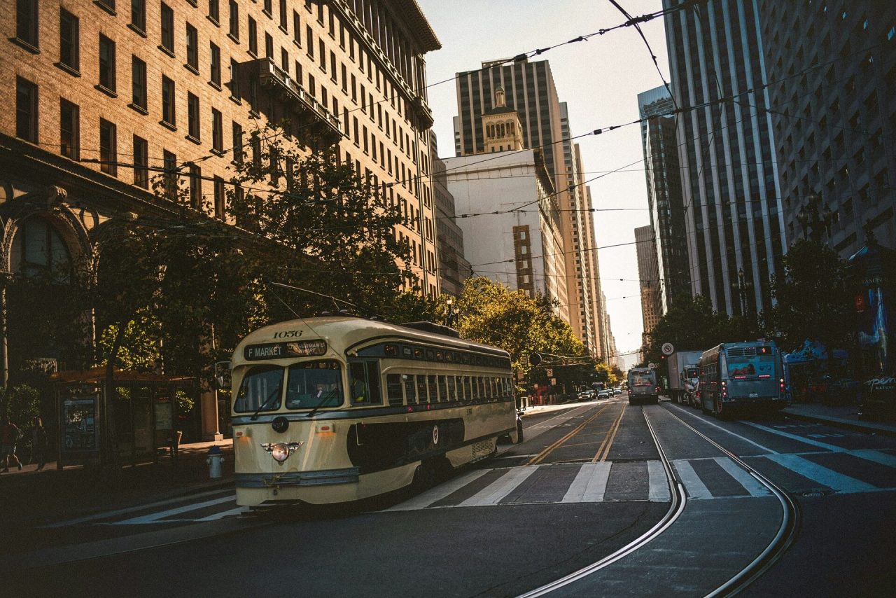 White public bus driving on a city street past modern high-rise buildings during daytime.